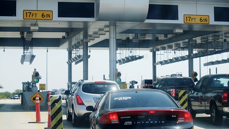 Vehicle lanes queue toward a covered land border inspection plaza with overhead signage and booths.