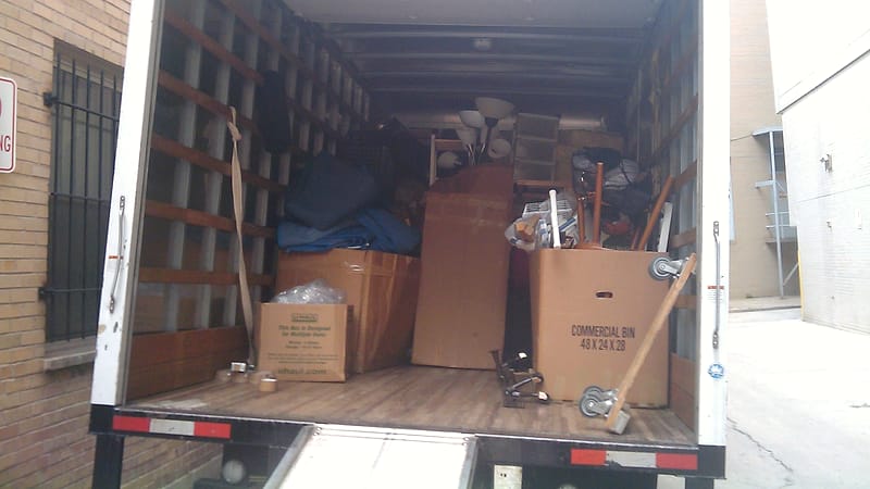 Stacked cardboard moving boxes and packing material fill the back of a household removal van.